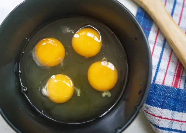 Top view of four eggs cracked into a black bowl beside a striped dish towel