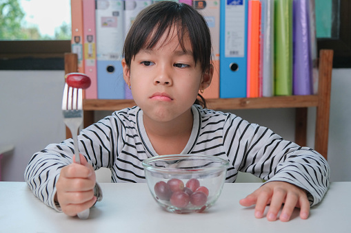 Children don't like to eat fruits. Cute young Asian girl refusing to eat healthy fruits. Nutrition and healthy eating habits for children.