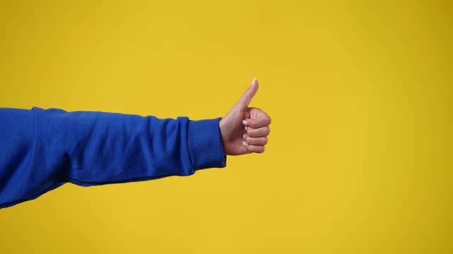 4k video of one girl hand who showing thumbs up over yellow background.