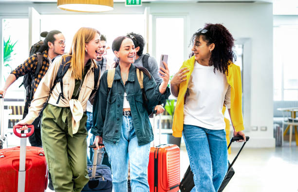 Multi racial diverse friends group arriving at hotel resort lobby with suitcases - Travel vacation life style concept with young people having fun before checkin time - Bright vivid backlight filter stock photo