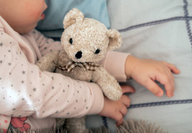 istock Close up little teddy bear hugging by infant sleeping girl. 1484813478