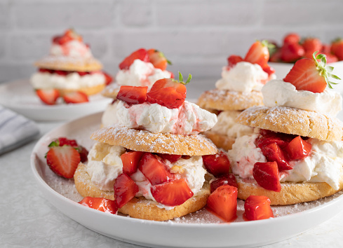 Traditional english strawberry shortcakes. Delicious summer pastry dessert. Served ready to eat on a white plate on light background. Front view