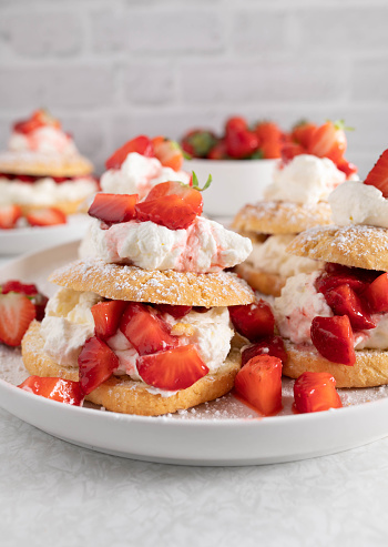 Fresh and homemade baked strawberry shortcakes with whipped vanilla cream and marinated strawberries. Served ready to eat on a white platter isolated on light kitchen counter. Closeup, front view with copy space