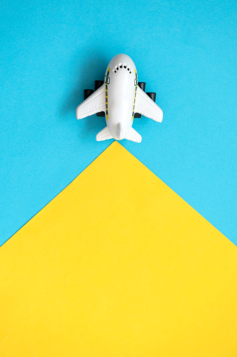 A toy airplane is flying on a yellow and blue background. Travel concept. Top view.