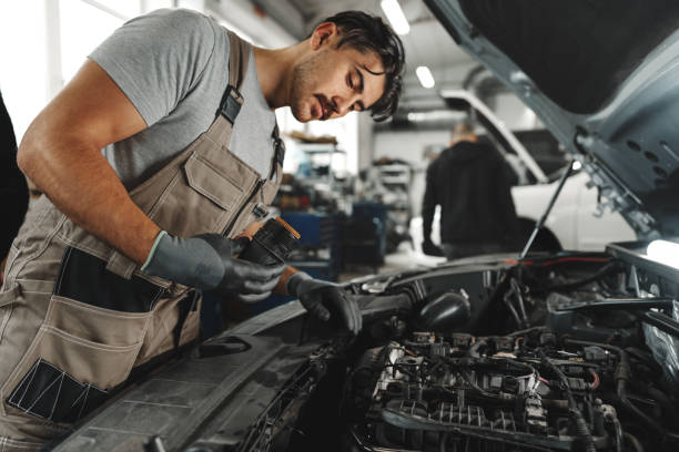 Young male mechanic examining engine under hood of car at the repair garage Young male mechanic examining engine under hood of car at the repair garage close up mechanic working under car stock pictures, royalty-free photos & images