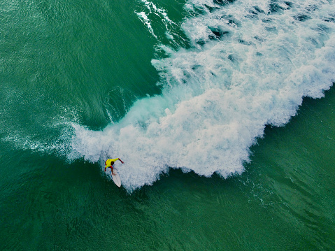 Person surfing at North Stradbroke Island. Surfer catching a wave at Cylinder Beach in Stradbroke Island, near Brisbane, in Queensland Australia. Aerial drone view of person on surf board catching a wave with wave breaking and clear blue turquoise water.