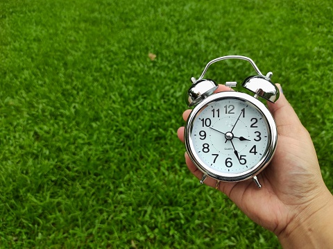 Antique silver alarm clock in human hand on blurred grass background.