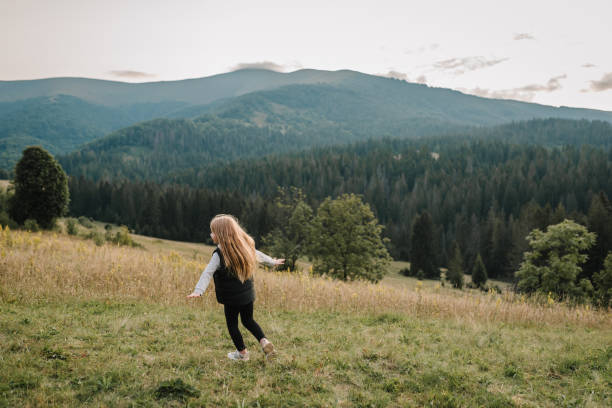 Child in autumn mountains. Girl is running on the grass in the field and enjoying nature. Little hiker and traveler walk on top of foggy mountain. World Tourism Day. Active outdoor games. Back view. niño en las montañas de otoño. la niña está corriendo sobre la hierba en el campo y disfrutando de la naturaleza. pequeño excursionista y viajero camina en la cima de la montaña brumosa. día mundial del turismo. juegos activos al aire libre. vista