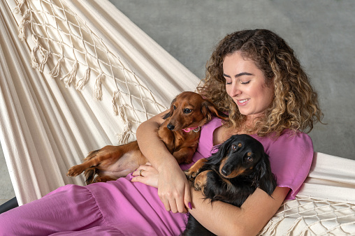 One woman resting in a hammock holding two Dachshund dogs on her lap