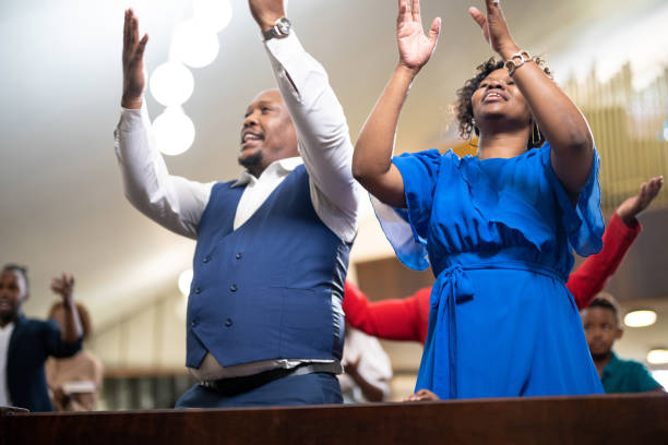 Couple singing and dancing with arms raised in church Multi-generation family and congregation enjoying church service black gospel church stock pictures, royalty-free photos & images
