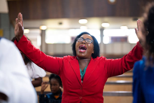 Woman in red jacket singing with arms outstretched in church Woman in red jacket singing with arms outstretched in church black female gospel singers stock pictures, royalty-free photos & images