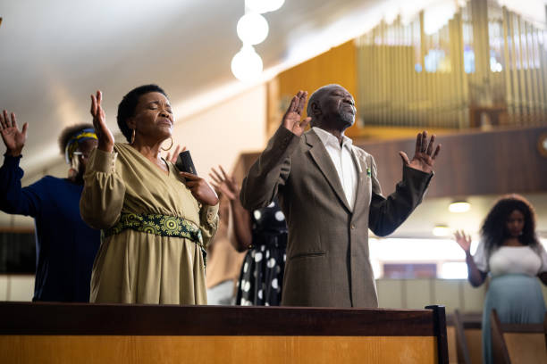 istock Seniors with hands raised standing praying in church 1484840463