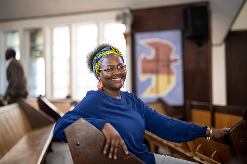 Candid portrait woman sitting on pew in church looking at camera