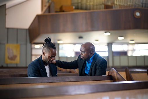 Pastor prays with man sitting in pew in church