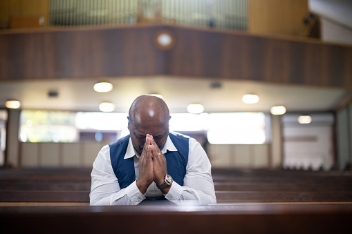 Front view man praying alone in church sitting in pew