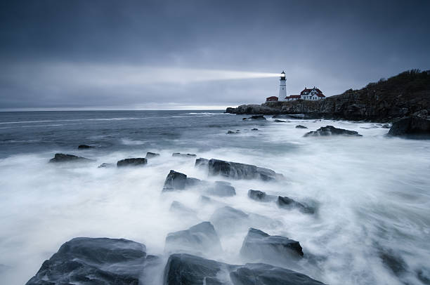 Dark seas lighthouse A long exposure of the waves washing over the rocks near the lighthouse at Portland Head, Maine. lighthouse stock pictures, royalty-free photos & images