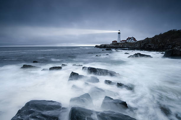 Dark seas lighthouse A long exposure of the waves washing over the rocks near the lighthouse at Portland Head, Maine. lighthouse storm night sea stock pictures, royalty-free photos & images