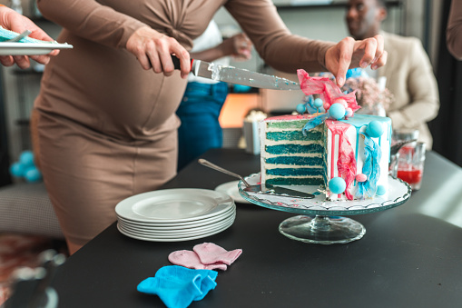 Close-up shot of an expectant mother sharing cake slices with a group of friends at a gender reveal party.