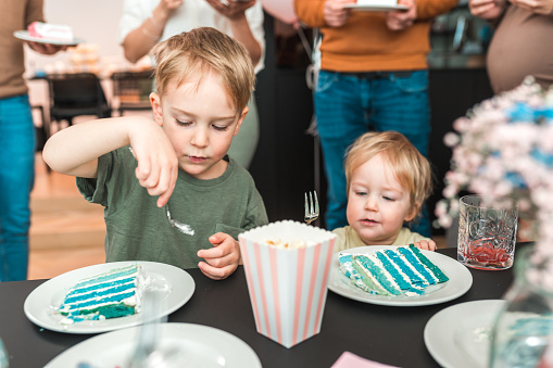 A delightful image of two young brothers eagerly enjoying a scrumptious cake at a gender reveal party.