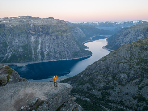 Female hiker standing on Trolltunga (troll tongue) famous rock high above a lake with panoramic view of the valley, popular tourist adventure trek in Norway