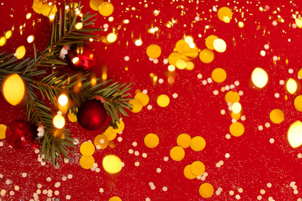 Branch of Christmas tree is decorated with red glass balls on red background. Bright backdrop with golden sparkles and round confetti. Branch of Christmas tree is decorated with red glass balls on red background. Bright backdrop with golden sparkles and round confetti. Blurred Christmas garland on foreground. Copy space. spectrum field stock pictures, royalty-free photos & images