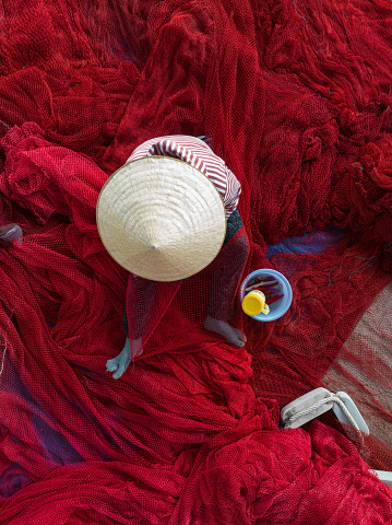 A woman is knitting net on a large beautiful red fishing net in Hon Ro dock, Nha Trang city, Khanh Hoa province, central Vietnam