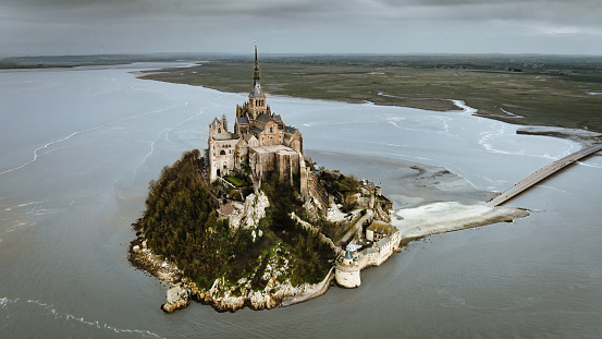 Mont Saint-Michel on tidal Island under cloudy and rainy skyscape. Aerial Drone Point of view Panorama from Atlantic Ocean Side over Mont Saint Michel towards the Normandy Coast. Stitched XXXL DJI Mavic 3 Panorama. Mont Saint-Michel, Avranches, Manche, Normandy, France, Europe
