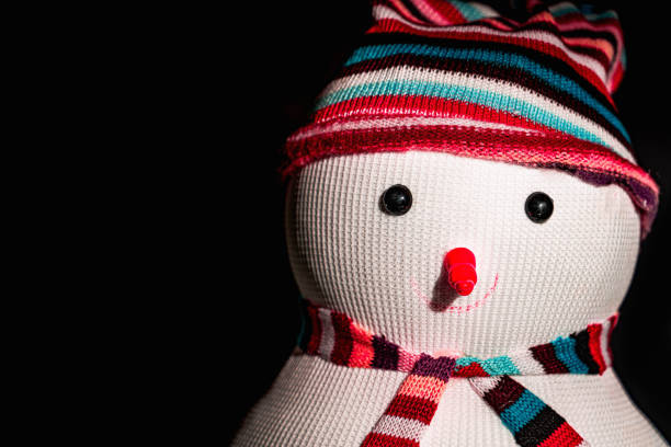 Snowman on a black background. High quality photo. Snowman's head in a hat, with a colored scarf on a black background