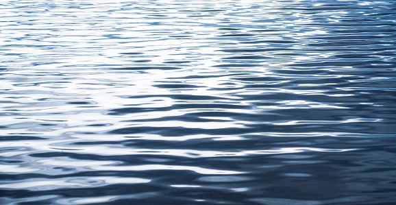 A pattern of gentle ripples on the surface of a wide body of water, with soft daylight reflected in the waves.