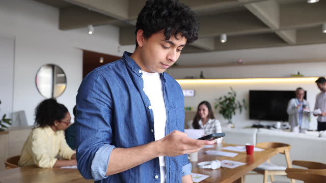 Latin American young man taking a break from work texting on smartphone cheerfully