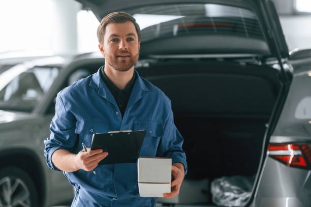 istock With notepad and box. Man in blue uniform is working in the car service 1484870288