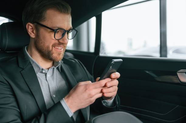 Holding smartphone. Man in formal business clothes is sitting in the modern automobile stock photo