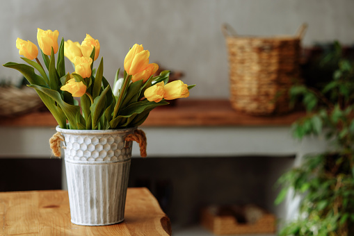 An indoor shot of a bouquet of yellow tulips in a kitchen interior on a wooden tabletop. Gift concept for March 8, valentines day or mothers day.