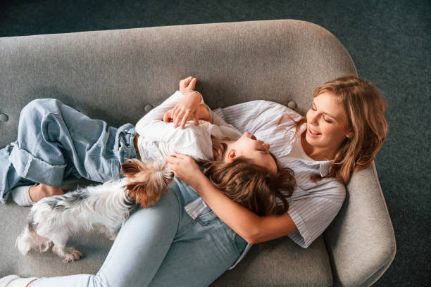 Lying down on the sofa. Mother with her daughter and with cute dog is in domestic room stock photo