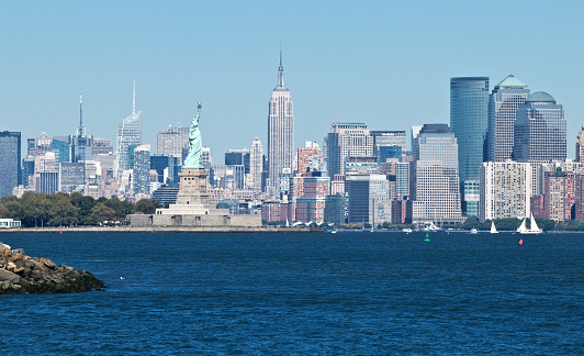 Surrounded by blue water, the Statue of Liberty faces the Manhattan skyline on a clear day.