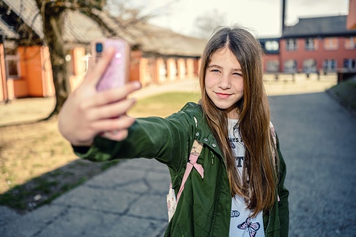 Smiling elementary school girl taking self portrait with their mobile phone