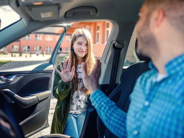 Father in car dropping off daughter in front of school gates stock photo