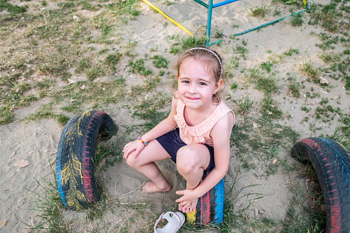 portrait of a little girl on a playground with tires and a posha sitting on them