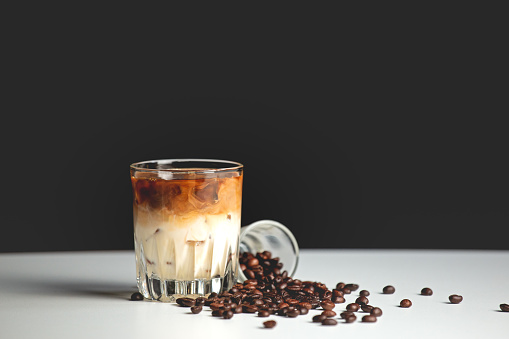 Glass of ice coffee latte with coffee beans on white table. Cold beverage in summer.