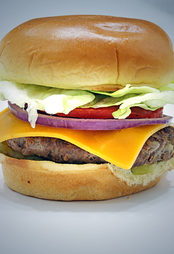 Cheese burger topped with cheddar, lettuce, tomato, dill pickle and red onion on a brioche bun full frame close up