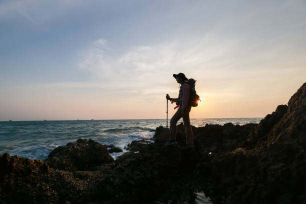 une randonneuse se tient sur la falaise rocheuse contre le coucher du soleil à seaview, silhouette de réussite de randonnée en montagne - rock climbing mountain climbing women achievement photos et images de collection