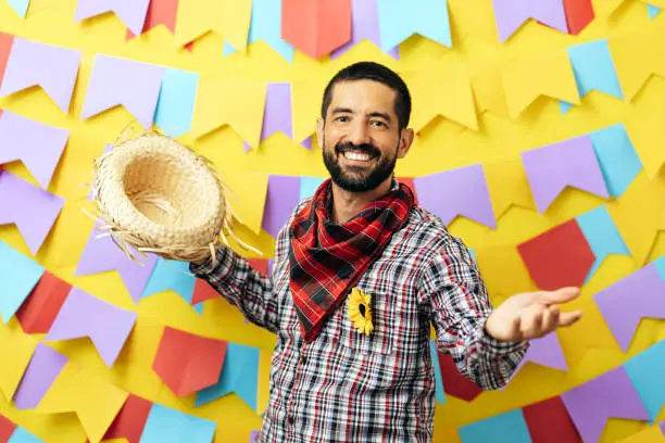 Photo of Brazilian man wearing traditional clothes for Festa Junina - June festival - over colorful background with pennants