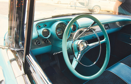 Front seat and steering wheel of a classic car viewed from outside the window looking in