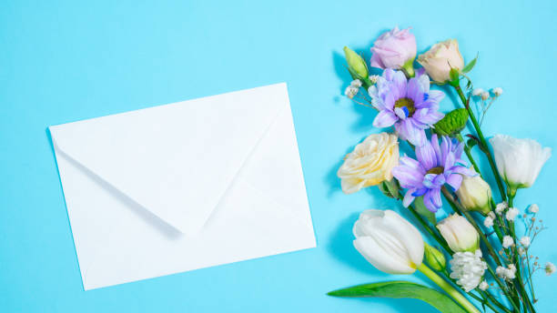 istock Natural flowers appear on blue background and form bouquet. White envelope appears next to it. 1484896329