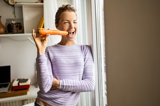Young Asian woman eating fresh organic food. Close-up of girl biting carrot. Healthy lifestyle concept