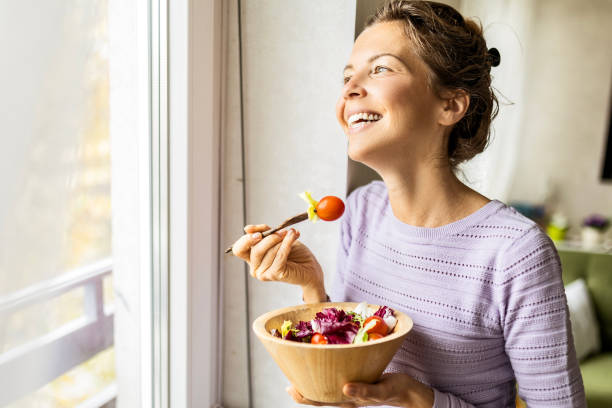 istock Young woman enjoying a delicious salad looking through window 1484898417