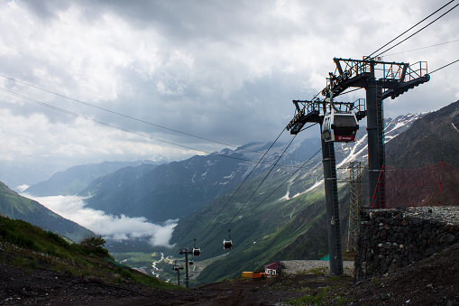 cableways moving up and down in the Elbrus high in the mountains against the background of snow-capped peaks and cloudy sky and copy space in Terskol, Kabardino-Balkaria in summer day
