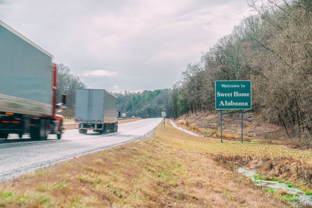 Two White Blank Semi Trucks Driving along I-65 South by the "Sweet Home Alabama" Sign on the Tennessee/Alabama Border in Winter Two White Blank Big Rig Trucks Driving on Interstate Highway 65 South by the "Sweet Home Alabama" Sign on the Tennessee / Alabama Border in Winter near Huntsville, AL tennessee road sign stock pictures, royalty-free photos & images