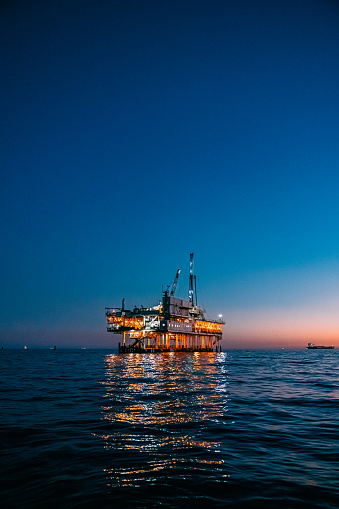 A stunning photograph of offshore oil drilling at sunset in Huntington Beach, California. The pink hues of the setting sun highlight the industrial machinery and equipment used in the drilling and extraction of fossil fuels, including crude oil and natural gas. 

This image captures the intersection of the energy industry and the natural beauty of the Pacific Ocean, and speaks to issues of fuel and power generation, energy crises, and environmental concerns surrounding the oil and gas industry.