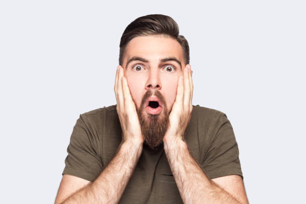 istock Man keeps hands on cheeks, looking at camera with big eyes, sees something amazing. 1484903455